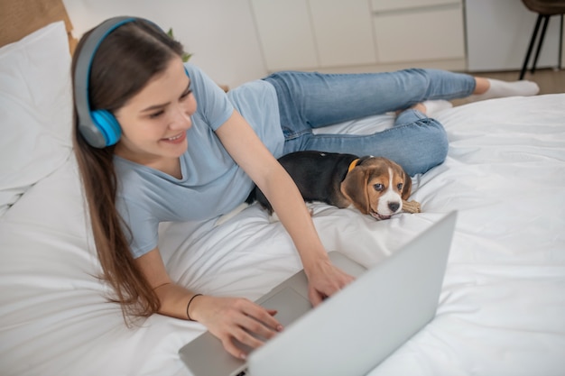 Chiot mignon allongé à côté de son propriétaire pendant qu'elle regarde quelque chose en ligne