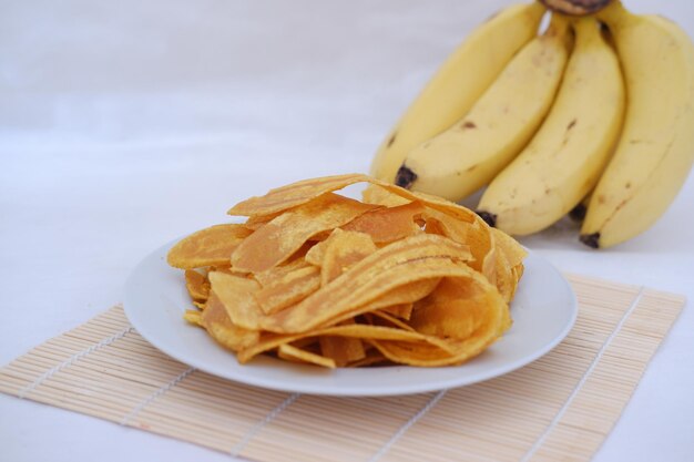 Chips de banane croustillantes sur une assiette blanche avec des bananes fraîches