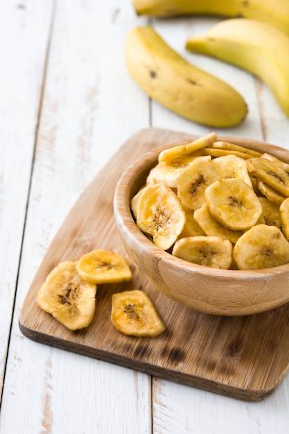 Chips de banane dans un bol sur une table en bois blanc