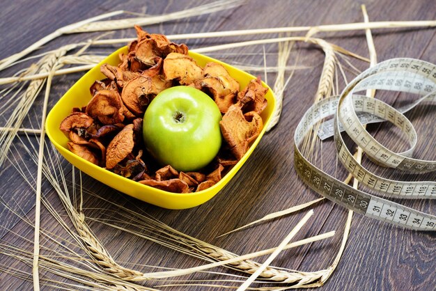 Chips à base de pommes dans une assiette jaune avec de la pomme verte et du spica de blé autour de l'espace de copie de la vue de dessus de table en bois