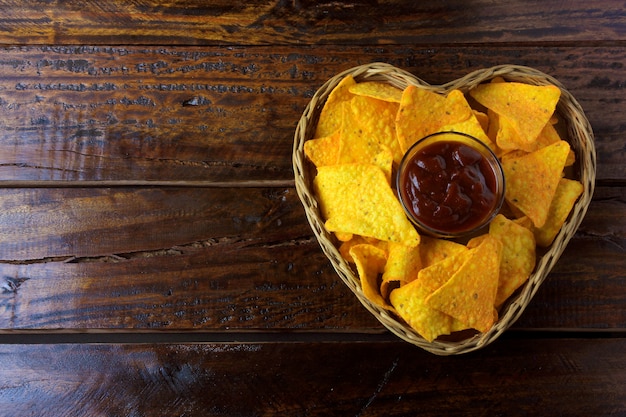 Chips de maïs Nachos avec sauces placées dans un panier en forme de coeur sur une table en bois