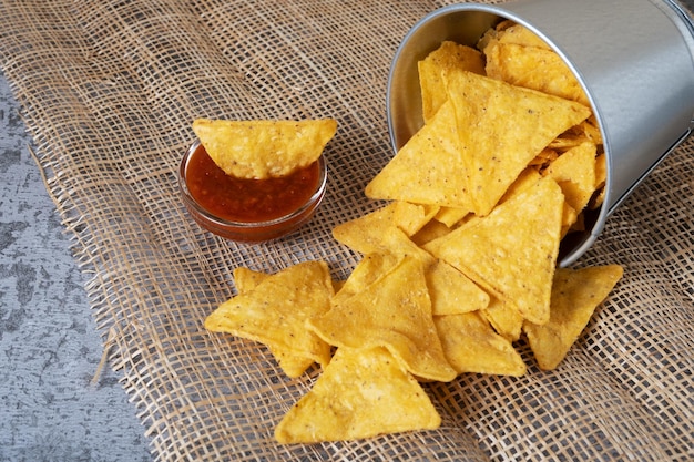 Chips de nacho de maïs déversées d'un seau en métal sur le fond d'une cornée tressée