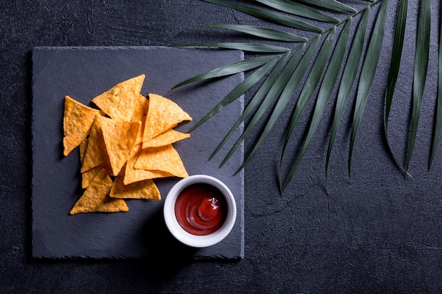 Chips nachos avec sauce chili et branche de palmier sur fond noir