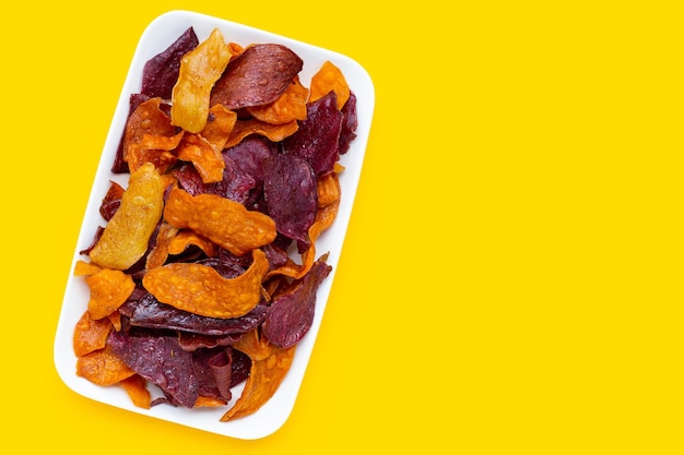 Chips de patates douces violettes et jaunes en plaque sur fond jaune.