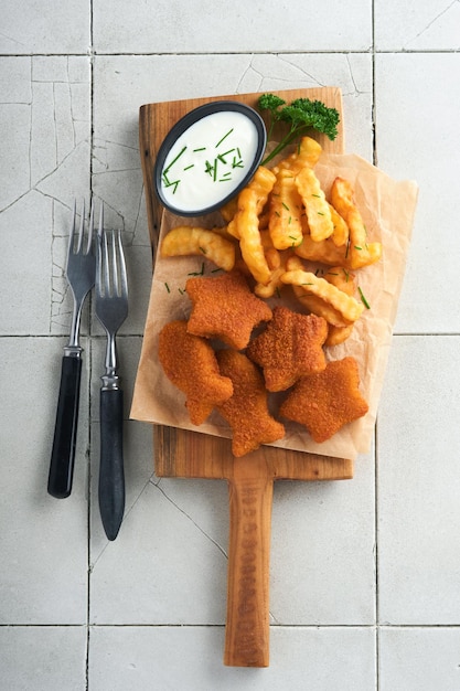 Chips de poisson restauration rapide britannique Bâtonnets de poisson avec frites set serveur sur planche rustique sur fond de table de comptoir en tuiles fissurées grises traditionnelles britanniques authentiques plats à emporter