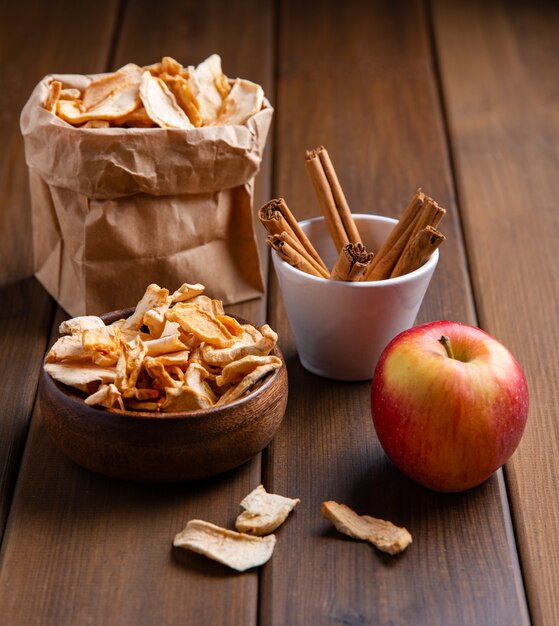 Chips de pommes maison sucrées séchées à la cannelle dans un bol en bois sur fond de bois