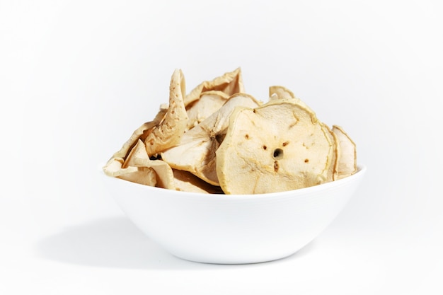 Chips de pommes sèches dans une assiette blanche isolée sur fond blanc. Nourriture déshydratée. Un tas de chips de pomme. Alimentation collation saine.