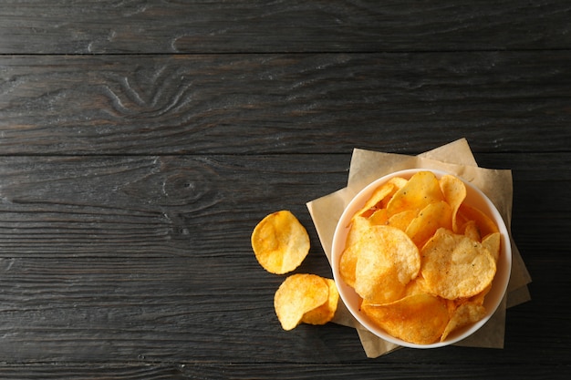 Chips de pommes de terre dans un bol, papier kraft sur bois, espace pour le texte. Vue de dessus