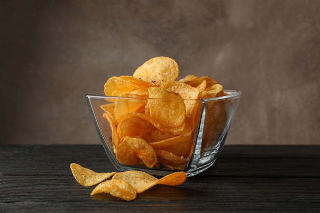 Chips de pommes de terre dans un bol en verre sur une table en bois, espace pour le texte