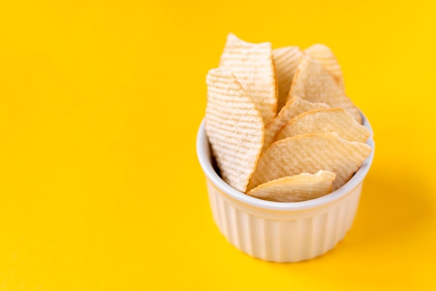 Chips de pommes de terre rayées dans un bol en céramique blanche sur fond jaune. Malbouffe malsaine, frites