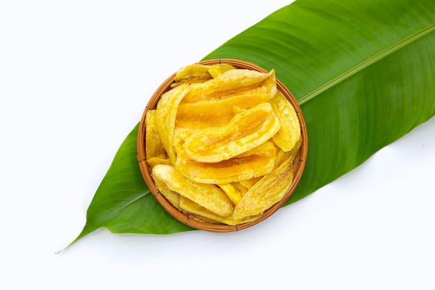 Chips de tranche de banane dans un panier de bambou sur feuille verte sur fond blanc.