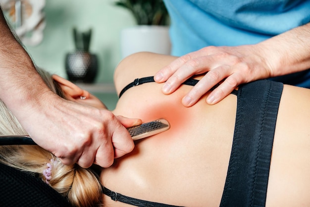 Chiropraticien effectuant des techniques de relâchement myofascial avec l'outil IASTM pour le muscle rhomboïde afin de soulager la douleur scapulaire