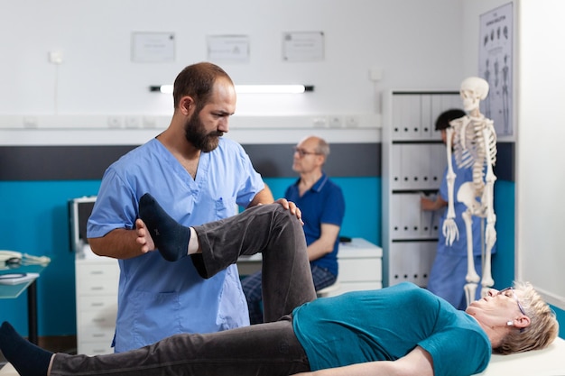 Chiropraticien étirant le muscle de la jambe pour soulager la pression pour la récupération d'une femme à la retraite. Assistant médical aidant un patient âgé souffrant de douleurs au genou, faisant de l'exercice physique pour la physiothérapie