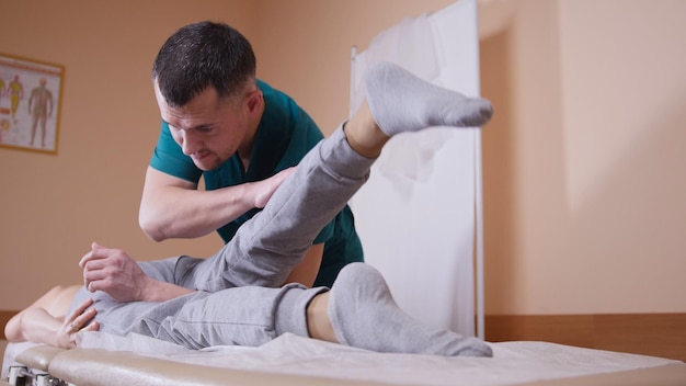 Chiropraticien massant une jeune femme allongée sur une table de massage, étirant et fléchissant son articulation de la hanche en appuyant sur son genou, concept de santé et médical