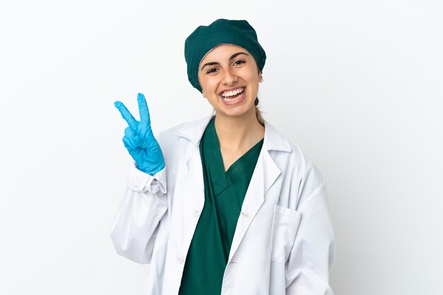 Chirurgien femme caucasienne isolée sur fond blanc souriant et montrant le signe de la victoire