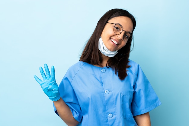 Chirurgien femme sur mur bleu heureux et en comptant quatre avec les doigts