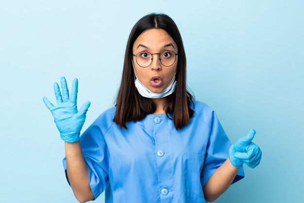 Chirurgien femme sur mur bleu isolé comptant six avec les doigts