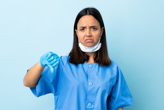 Chirurgien femme sur mur bleu montrant le pouce vers le bas avec une expression négative