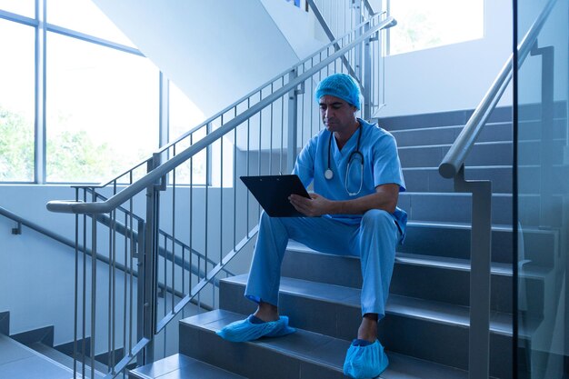 Photo chirurgien masculin écrivant sur un bloc-notes alors qu'il est assis sur les escaliers de l'hôpital