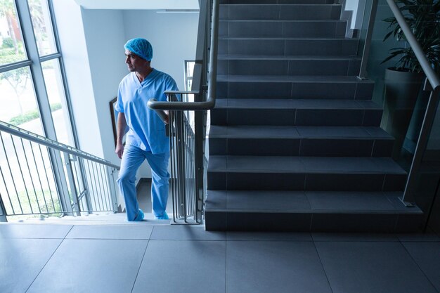 Photo chirurgien masculin regardant par la fenêtre en montant les escaliers de l'hôpital