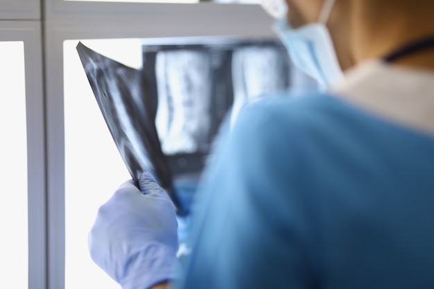 Un chirurgien masculin se tient dans le bureau et regarde la radiographie arrière voir le médecin avec soin