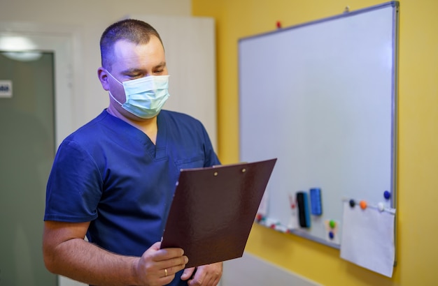 Chirurgien masculin sérieux avec masque debout au bureau avec dossier.