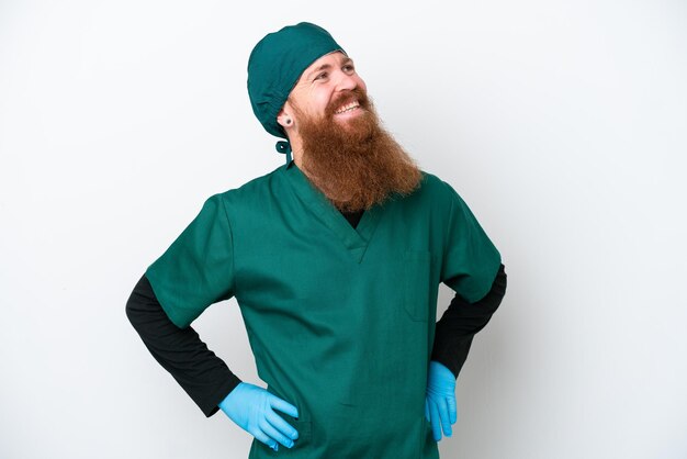 Chirurgien rousse homme en uniforme vert isolé sur fond blanc posant avec les bras à la hanche et souriant