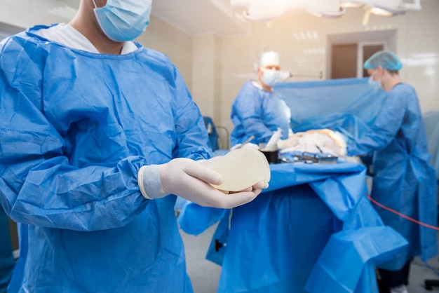 Chirurgien en salle d'opération tient un implant mammaire stérile en silicone dans les mains