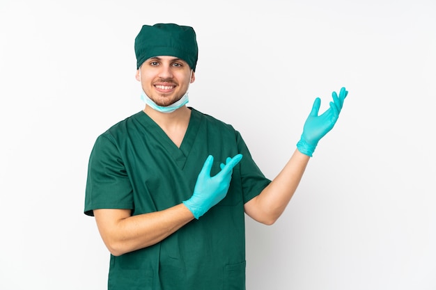 Chirurgien en uniforme vert isolé sur un mur blanc isolé, tendant les mains sur le côté pour inviter à venir