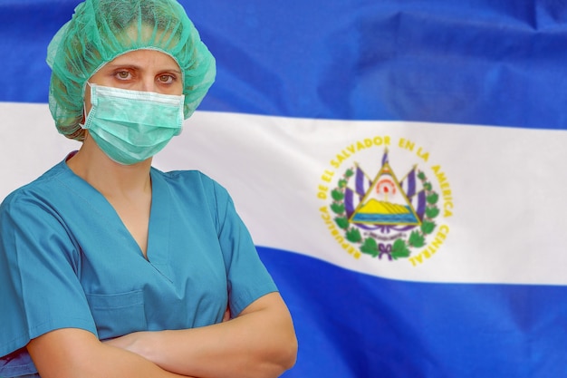 Chirurgienne en masque et chapeau regarde la caméra sur le fond du drapeau d'El Salvador