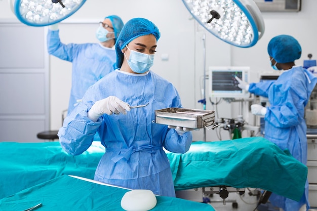 Une chirurgienne en uniforme chirurgical prenant des instruments chirurgicaux en salle d'opération Une jeune femme médecin en chambre d'opérations de l'hôpital