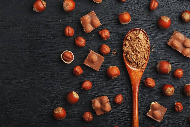 Chocolat aux noisettes et une cuillère en bois au cacao, entourée de noix dans la coque et pelée.