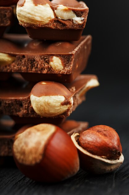 Chocolat aux noisettes en forme de tour sur fond sombre, entouré de noix en coque et pelé.