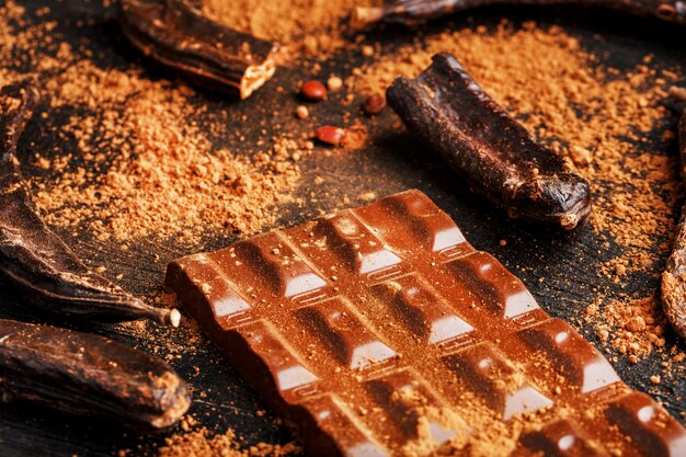 Chocolat de caroube et poudre de fruit de caroube sur une surface sombre