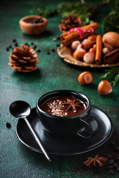 Chocolat chaud à l'anis et noix dans une tasse en céramique noire sur une vieille surface de béton vert foncé. Mise au point sélective.