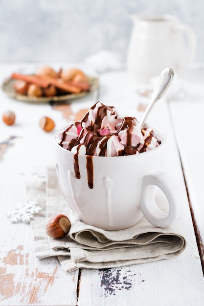 Chocolat chaud avec des bonbons à la guimauve dans une tasse en céramique rustique blanche sur une vieille surface en bois clair. Mise au point sélective.