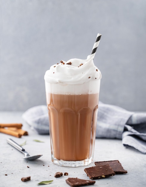 Chocolat chaud avec crème fouettée et cannelle dans un grand verre sur fond bleu Vue de face et espace de copie