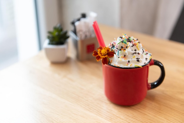 Chocolat chaud avec de la crème fouettée dans une tasse rouge sur une table en bois