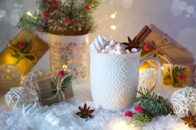 Chocolat chaud dans une tasse blanche avec des guimauves et des cadeaux de Noël sous la lumière vive. Boisson de Noël.