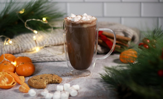 chocolat chaud dans une tasse en verre avec des mini guimauves sur une table grise, arrière-plan flou de noël