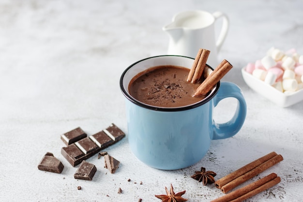 Chocolat chaud épicé à la cannelle et à l'anis étoilé dans une tasse bleue émaillée sur fond blanc