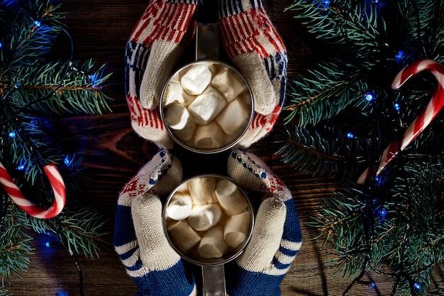 Chocolat chaud fait maison de Noël avec des guimauves dans les mains de l'homme et de la femme vue de dessus