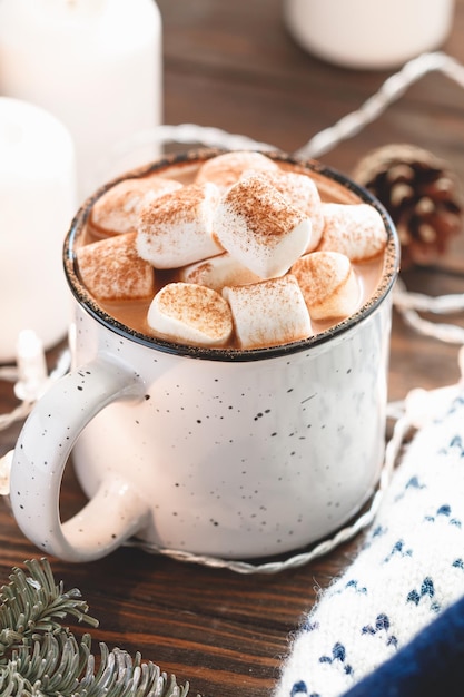 Chocolat chaud avec guimauve dans une tasse en céramique blanche parmi les choses d'hiver et décor sur une table en bois Le concept de vacances douillettes et du Nouvel An