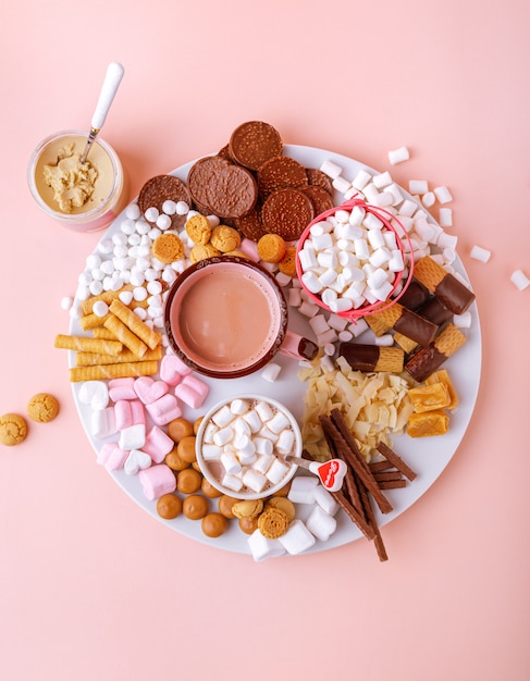 Chocolat chaud, guimauves, chocolats et biscuits sur tableau rose