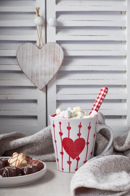 Chocolat chaud avec des guimauves, coeur rouge sur la tasse sur la table avec des décorations d'hiver