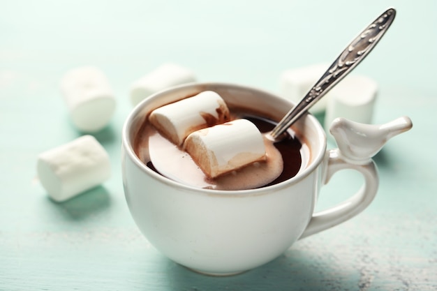 Chocolat chaud avec des guimauves dans une tasse, sur fond de bois de couleur