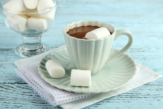 Chocolat chaud avec des guimauves dans une tasse, sur une table en bois de couleur, sur fond clair