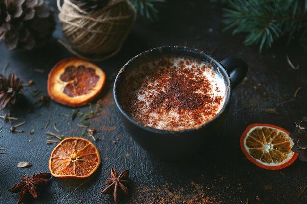 Chocolat chaud de Noël dans une tasse noire avec des oranges caramélisées, des branches de sapin et de la canne à sucre sur fond sombre, mise au point sélective