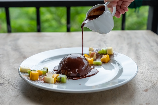 Chocolat chaud versé sur un dôme de cacao avec des tranches de fruits