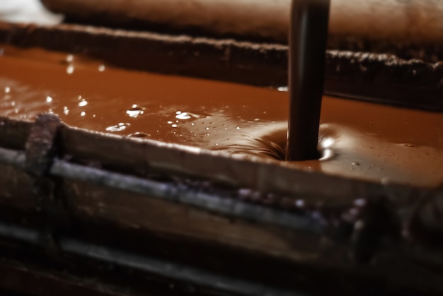 Le chocolat fondu chaud est versé dans un plateau dans une usine de confiserie, en gros plan